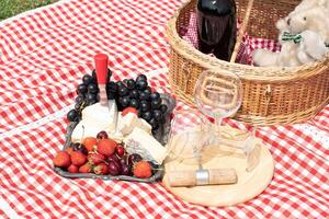 Sommer- Picknick auf ein Grün Rasen mit rot Wein, Käse und frisch Beeren, Trauben foto