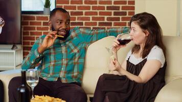 Paar reden auf Couch, verbrauchen Getränke und Snacks beim Sozial Wiedervereinigung nach fangen oben mit Freunde. afrikanisch amerikanisch Mann und Freundin genießen nett Gespräch, klatschen Über andere Gäste foto