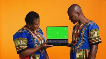 ethnisch Paar präsentieren Laptop mit grüner Bildschirm Anzeige, präsentieren isoliert Copyspace Vorlage und posieren auf Kamera. afrikanisch amerikanisch Mann und Frau zeigen beim leer Attrappe, Lehrmodell, Simulation Layout. foto