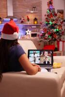 Frau feiern Weihnachtszeit mit Fernbedienung freunde während online Videoanruf Treffen Konferenz Telearbeit ruhen auf Couch im Weihnachten dekoriert Küche. Erwachsene Person genießen Weihnachten Urlaub foto