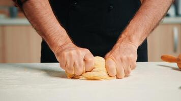 schließen oben von kaukasisch alt Koch Mann Gestaltung ein Brot Laib. im Ruhestand Alten Bäcker mit Küche Uniform Mischen Zutaten mit gesiebt Weizen Mehl kneten zum Backen traditionell Kuchen und Brot foto