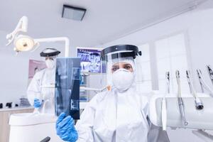 geduldig pov suchen beim Zahnarzt zeigen Röntgen Bild im Dental Büro. Stomatologie Spezialist tragen schützend Hazmat passen gegen Coroanvirus zeigen Radiographie. foto