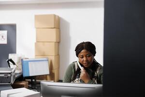 Lager Zimmer Mitarbeiter haben Fernbedienung Diskussion mit Kunde während Lagerhaus Inventar. afrikanisch amerikanisch Supervisor Analysieren Fan-Shop Logistik auf Computer, vorbereiten Klient bestellen foto