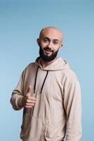 lächelnd arabisch Mann ausdrücken Befriedigung mit Daumen oben Geste Porträt. jung glücklich gut aussehend Person mit sorglos Emotionen zeigen die Genehmigung und Zustimmung während suchen beim Kamera foto