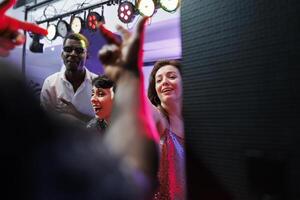 jung Musiker durchführen während Menge Jubel beim Nachtclub Leben Musik- Party. dj und Sänger Gruppe spielen auf Bühne beleuchtet mit Scheinwerfer während Menschen Tanzen beim Disko Versammlung foto