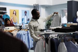 afrikanisch amerikanisch Mann wählen Jogger Hose im Einkaufszentrum Abteilung bekleidung Boutique. Kleidung Geschäft Kunde halten Sport Hose, Prüfung Stil und Größe Vor Herstellung Kauf foto