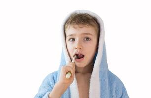 klein Kind, Junge im ein Blau Frottee Kleid mit ein Zahnbürste auf Weiß. ein Kind Bürsten seine Zähne. Gesundheitswesen und Dental Pflege foto