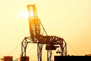 Nahansicht und Silhouette von Container Kran sind Wird geladen Behälter von Ladung Schiff beim Osaka Hafen auf Abend mit Sonnenuntergang Farbe Ton und Sonne Fackel Hintergrund. foto