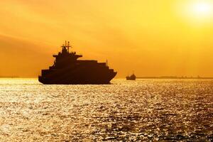 Silhouette von Ladung Schiff mit voll Schiffsladung Ladung Behälter sind Segeln im das Osaka Bucht Abend mit Sonne Fackel Hintergrund. foto