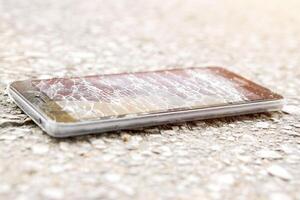 Nahansicht schwarz Handy, Mobiltelefon Telefon Unfall fallen zu das Straße und Glas gebrochen mit Sonne Fackel Hintergrund. foto