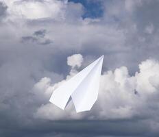 Weiß Papier Flugzeug im ein Blau Himmel mit Wolken. das Botschaft Symbol im das Bote foto