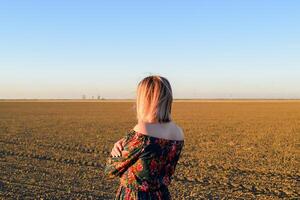 Frau im ein gepflügt Feld im ein rot schwarz Kleid auf ein Sonnenuntergang Hintergrund. foto