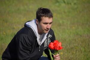 ein Mann im ein Jacke auf ein Feld von Tulpen. Lichtung mit Tulpen. ein Mann ist reißen Tulpen im ein Strauß foto