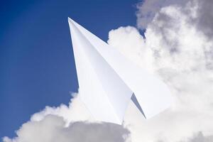 Weiß Papier Flugzeug im ein Blau Himmel mit Wolken. das Botschaft Symbol im das Bote foto