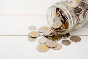 Neu thailändisch baht Münzen verschütten von ein Glas Krug, auf Weiß hölzern Tisch. Geschäft und Finanzen Konzept. foto