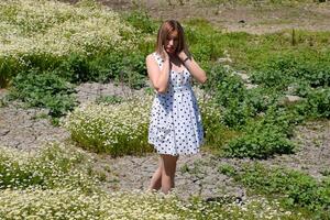 ein Frau im ein Weiß Kleid mit Polka Punkte ist auf ein Lichtung mit Gänseblümchen. Blühen Gänseblümchen foto