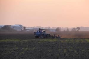 Traktor Pflügen Pflug das Feld auf ein Hintergrund Sonnenuntergang foto