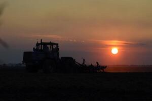 Traktor Pflügen Pflug das Feld auf ein Hintergrund Sonnenuntergang. Traktor Silhouette auf Sonnenuntergang Hintergrund foto