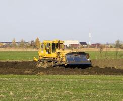 das Gelb Traktor mit befestigt grederom macht Boden Nivellierung. foto