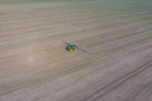 Traktor mit aufklappbar System von Sprühen Pestizide. düngen mit ein Traktor, im das bilden von ein Aerosol, auf das Feld von Winter Weizen. foto