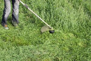 Anwendung Trimmer. Mähen Grün Gras mit ein Angeln Linie Trimmer foto