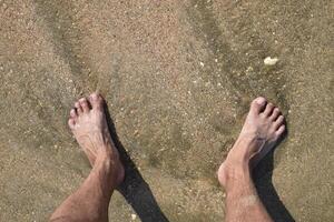 Beine Männer auf das Meer Sand in der Nähe von Meer Welle foto