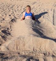 Mädchen im ein Bikini auf das Strand begraben im Hälfte im das Sand. foto