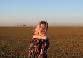 Frau im ein gepflügt Feld im ein rot schwarz Kleid auf ein Sonnenuntergang Hintergrund. foto