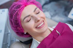 schön Frau mit gesund Gerade Weiß Zähne Sitzung beim Dental Stuhl mit öffnen Mund während ein Dental Verfahren. Dental Klinik. Stomatologie foto