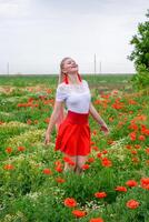 blond jung Frau im rot Rock und Weiß Shirt, rot Ohrringe ist im das Mitte von ein Mohn Feld. foto