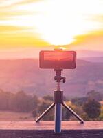 ein Smartphone ist Aufzeichnung das Sonne Rahmen Über ein Berg Bereich. foto