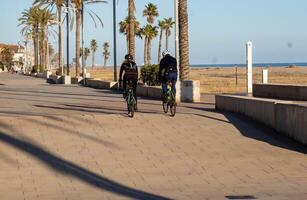 Comarruga, Tarragona, Spanien - - Februar 13, 2024. Paar von jung Radfahrer, nehmen Vorteil von das gut Wetter im Estragona zu Übung auf ein Fahrrad foto