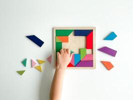 Kinder Hand sammelt mehrfarbig hölzern Mosaik auf Weiß Hintergrund. Kind löst bunt Tangram foto