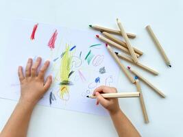 klein Kind zeichnet mit farbig Bleistifte auf Papier auf Weiß Tisch. foto
