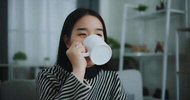 Porträt von entspannend jung Frau halten Tasse genießen Geruch Kaffee oder Tee und Trinken mit Glück im Morgen während sitzen auf Sofa im Leben Zimmer, frei Zeit, nimm brechen im Zuhause, lächelnd foto