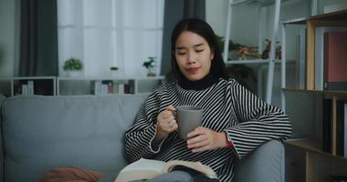 Porträt von glücklich jung asiatisch Frau Trinken Morgen Kaffee oder Tee und lesen im Leben Zimmer beim Zuhause auf Wochenende. Freizeit und Lebensstil, kostenlos Zeit foto