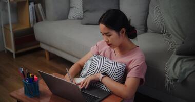 Porträt von jung Frau Sitzung auf das Fußboden gelehnt gegen ein Sofa Arbeiten mit ein Laptop und nehmen Anmerkungen im ein Notizbuch beim Zuhause Büro. foto