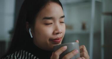 Porträt von glücklich jung asiatisch Frau genießen Hören zu das Musik- mit kabellos Kopfhörer während Sitzung trinken Kaffee auf Sofa im Leben Zimmer beim heim, Freizeit und Lebensstil, kostenlos Zeit foto