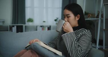 Porträt von glücklich jung asiatisch Frau Trinken Morgen Kaffee oder Tee und lesen im Leben Zimmer beim Zuhause auf Wochenende. Freizeit und Lebensstil, kostenlos Zeit foto