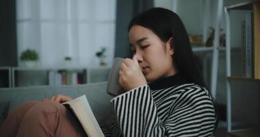 Porträt von glücklich jung asiatisch Frau Trinken Morgen Kaffee oder Tee und lesen im Leben Zimmer beim Zuhause auf Wochenende. Freizeit und Lebensstil, kostenlos Zeit foto