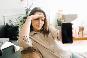 unzufrieden tausendjährig Frau halten Smartphone mit leer Bildschirm, ausdrücken Stress und Unzufriedenheit im modern Technologie verwenden foto