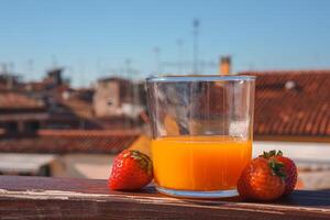 erfrischend Glas von Orange Saft mit Erdbeere auf Balkon mit Blick auf Venedig foto