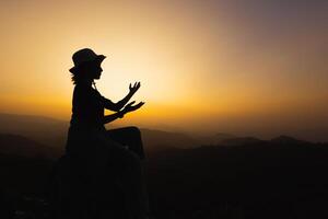 silhuette junge Frau, die auf dem Berg betet, die Arme ausgestreckt und einen wunderschönen, dramatischen Sonnenaufgang beobachtet. foto