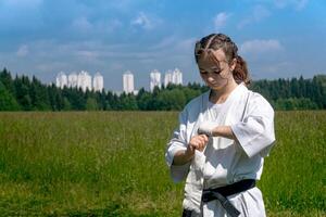 Teenager Mädchen im ein Kimono Verpackung ein Handgelenk wickeln um ihr Hand Vor nehmen Karate draußen foto