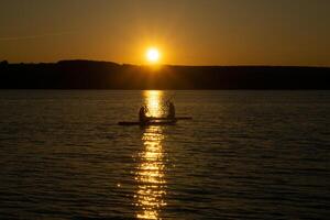 zwei Surfer auf aufstehen Paddleboards gegen das Hintergrund von das Rahmen Sonne foto