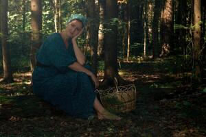 jung Frau im Volk Bauer Kleider mit ein Korb zum Sammeln wild Pflanzen sitzt auf ein Log im das Nadelbaum Wald foto