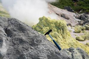 geologisch Hammer im das Felsen gegen das Hintergrund von ein dämpfen Fumarole auf das Steigung von ein Vulkan foto