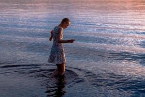 Teen Mädchen im ein Kleid durch das Meer tritt ein das Wasser foto