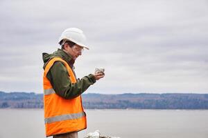 Geologe oder Bergbau Ingenieur untersucht ein Stichprobe von ein Mineral von ein Talus auf ein Fluss Bank foto