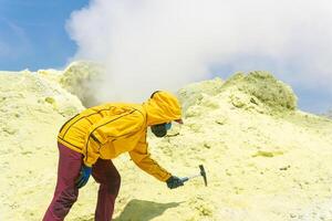 weiblich Vulkanologe auf das Steigung von ein Vulkan Nächster zu ein Rauchen Fumarole nimmt ein Stichprobe von ein Mineral von das Kante von ein schwefelhaltig Krater foto